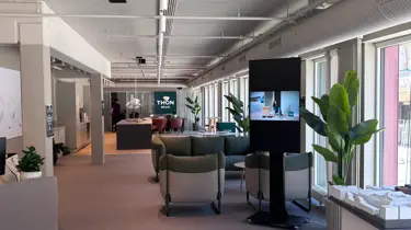 Lyst og moderne visningssenter for boligprosjektet Dronningkvartalet fra Thon Bolig med sittegrupper, store vindusflater, grønne planter, digital informasjonsskjerm og boligmodell utstilt i forgrunnen.