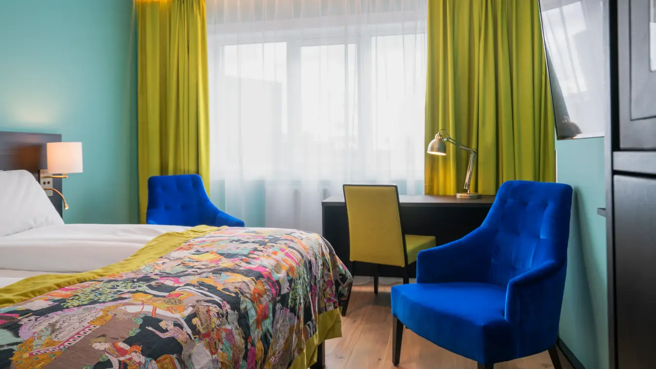 Twin room med hvit sengetøy, gule gardiner, skrivepult og blå lenestol på Thon Hotel Europa i Oslo sentrum rett ved Slottsparken