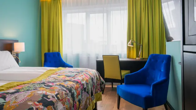 Twin room med hvit sengetøy, gule gardiner, skrivepult og blå lenestol på Thon Hotel Europa i Oslo sentrum rett ved Slottsparken