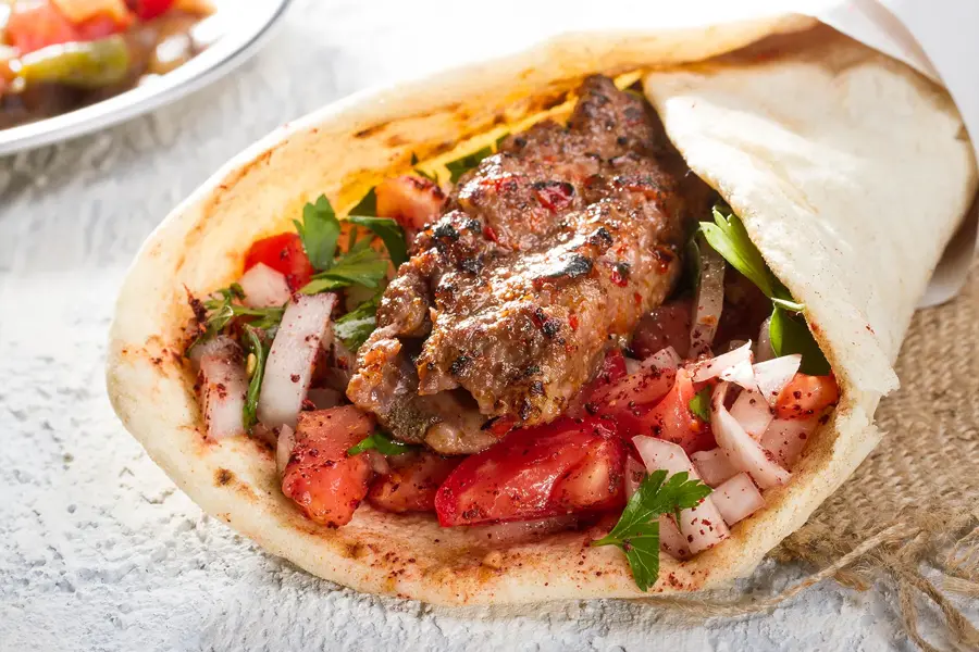 Tyrkisk og arabisk tradisjonell Ramadan Adana kebab rulle wrap servert med yoghurt, auberginesalat og hete peppersyltede agurker på rustikt trebrett.