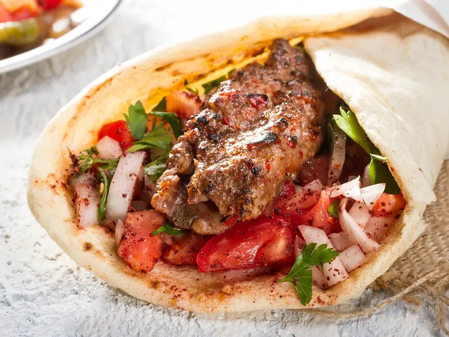 Tyrkisk og arabisk tradisjonell Ramadan Adana kebab rulle wrap servert med yoghurt, auberginesalat og hete peppersyltede agurker på rustikt trebrett.