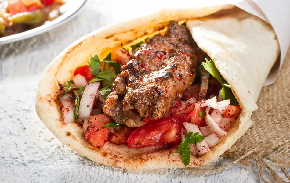 Tyrkisk og arabisk tradisjonell Ramadan Adana kebab rulle wrap servert med yoghurt, auberginesalat og hete peppersyltede agurker på rustikt trebrett.