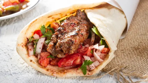 Tyrkisk og arabisk tradisjonell Ramadan Adana kebab rulle wrap servert med yoghurt, auberginesalat og hete peppersyltede agurker på rustikt trebrett.