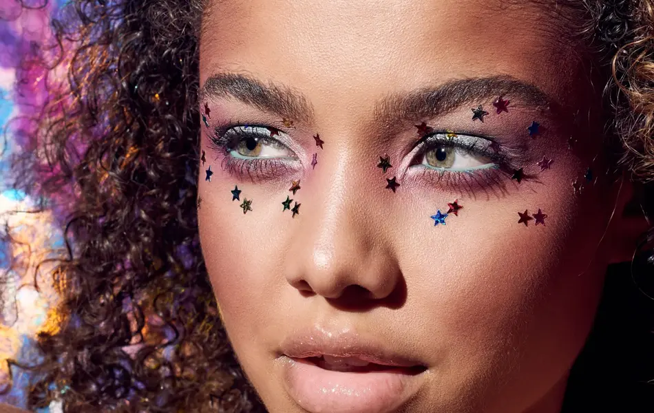 Kvinne med afro poserer, har små stjerner rundt øynene og lilla øyenskygge