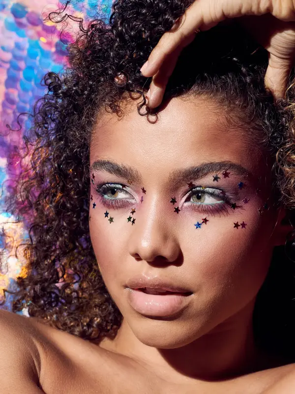 Kvinne med afro poserer, har små stjerner rundt øynene og lilla øyenskygge