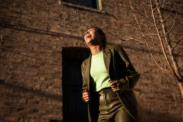 Dame med grønn jakke og bukse og lys grønn topp ler og ser opp mot himmelen utendørs