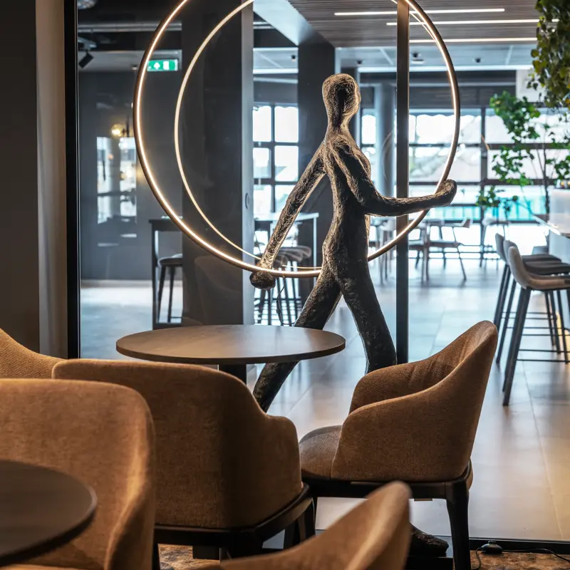 Utsnitt fra møterom med lite bord og stoler rundt. Stort vindu ut i lobby med en statue foran vindu.
