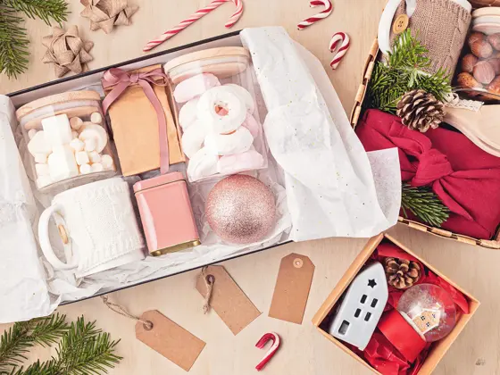 Preparing care package, seasonal gift box with marshmallow, tea,coffee or cacao box and christmas ornament. Personalized eco friendly basket for winter holidays. Top view, flat lay