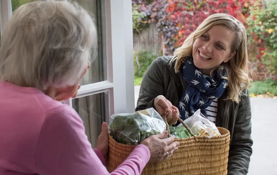 Dame som gir en annen dame en kurv med mat