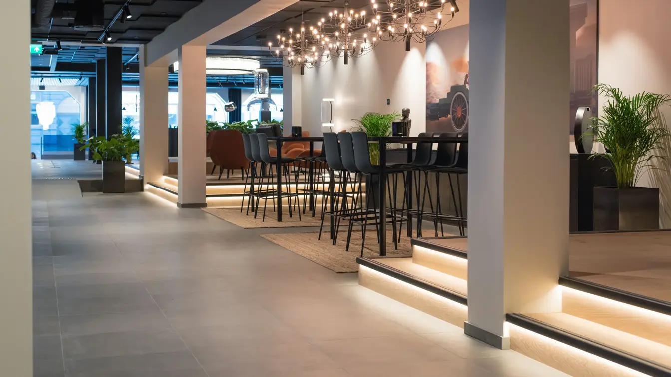 Luftig rom med mørke høye bord og stoler, grønne vekster og lysekroner i taket.  I lobbyen på Thon Hotel Norge i Kristiansand.