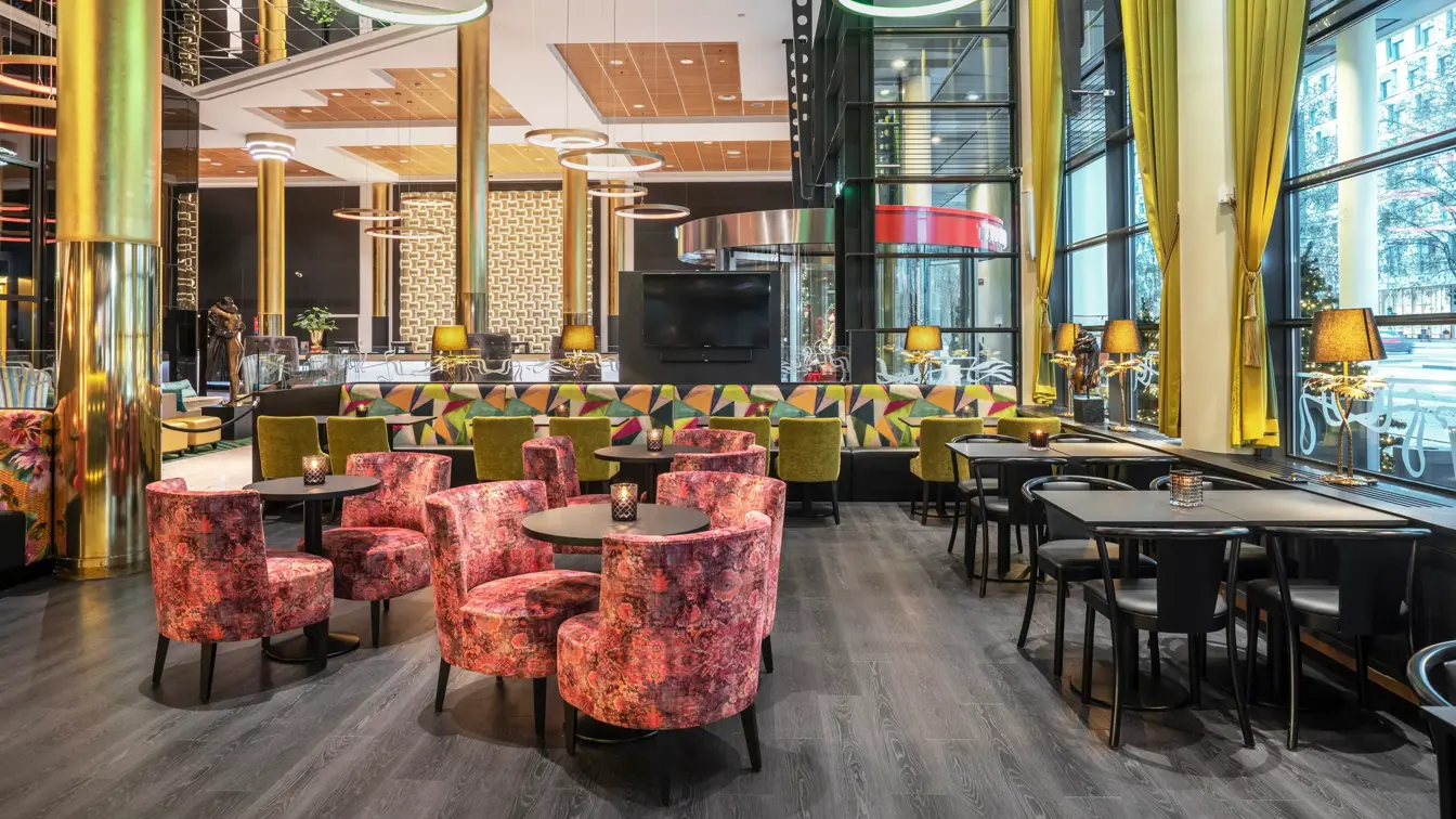 Svart gulv, vindu, gule gardiner, svarte bord, rosa stoler, svarte stoler, høyt under taket.