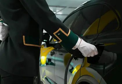 Ansatt i uniform og hvite hansker holder i en el-bil lader som står i en mørk bil