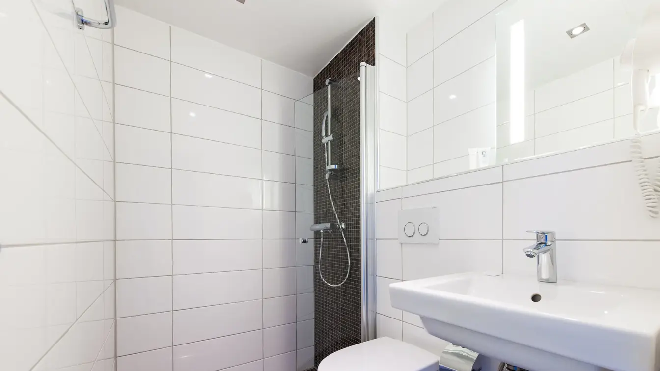 Brune gulvfliser, hvite veggfliser, toalett, vask.