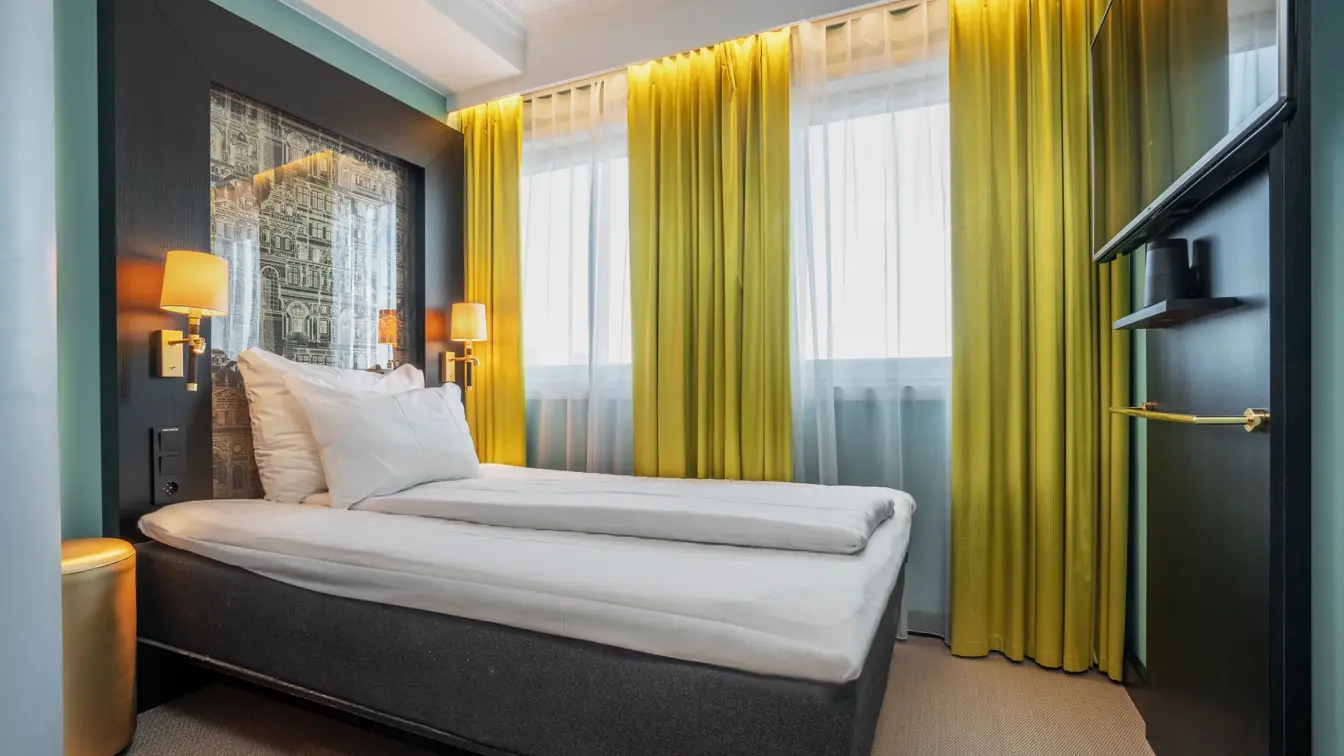 Enkeltrom med enkeltseng, sengelamper på hver side, gule gardiner, vegghengt TV