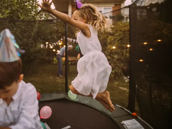 Jente og gutt med bursdagshatt hopper på trampoline fylt med ballonger