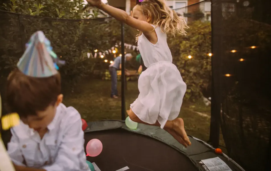 Jente og gutt med bursdagshatt hopper på trampoline fylt med ballonger