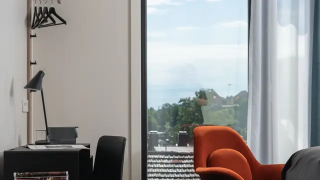 Stort vindu med en oransje stol foran, sort skrivebord og stol med leselampe i business rom på Thon Hotel Norge i Kristiansand