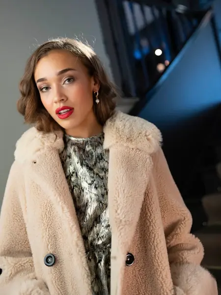 Damemodell med sølvglitrende topp og hvit teddykåpe.