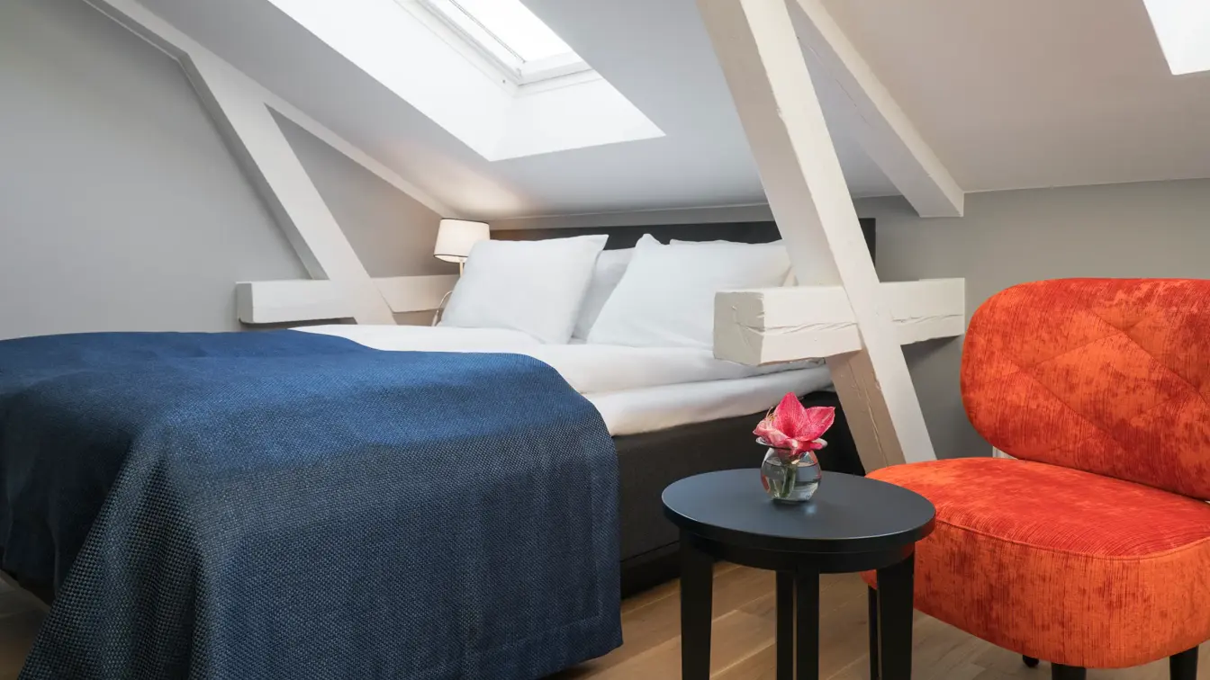 Dobbeltseng med orange stol og skråtak i standard double room på Thon Hotel Spectrum i Oslo sentrum