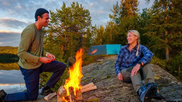 Mann og dame som tenner bål ved ett vann