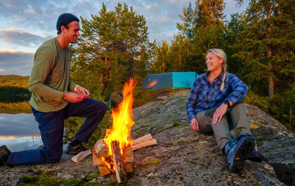 Mann og dame som tenner bål ved ett vann