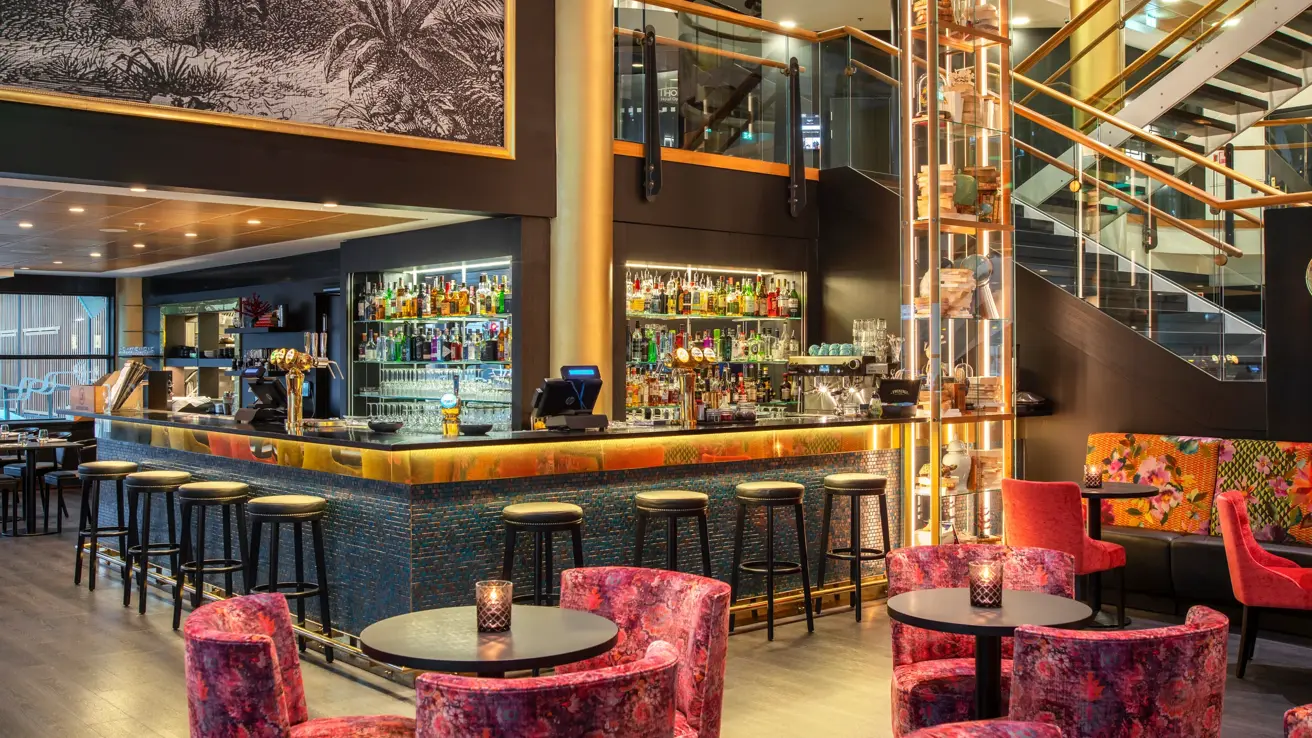 Bar, diverse sittegrupper med rosa stoler, bar midt i sentrum med barstoler. 