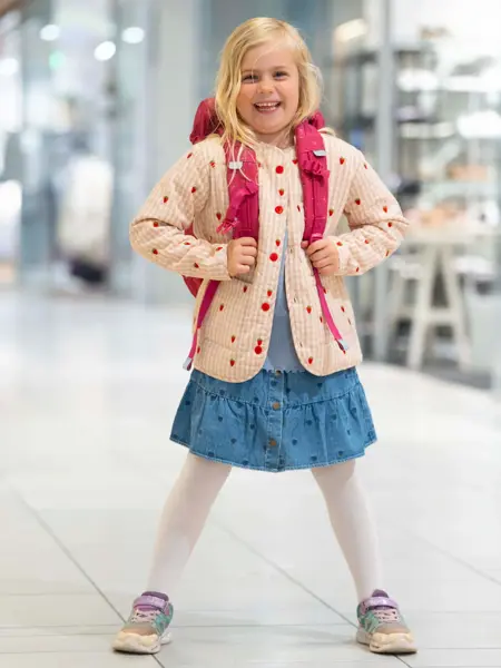 Jente med jakke, skjørt, strømpebukse, sneakers og rosa skolesekk
