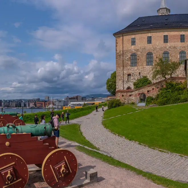 Utsikt over Akershus Festning en sommerdag. Kanoner i front og Tjuvholmen i bakgrunnen.