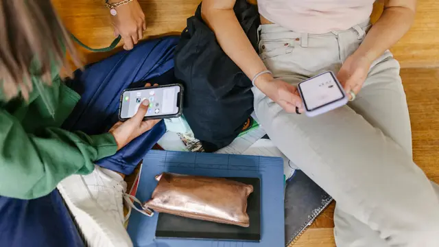 Fugleperspektiv på to personer som sitte med mobiler, skolesaker ligger rundt dem. Foto til artikkel om tips til åttende klasse.