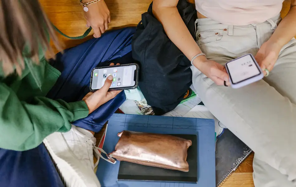 Fugleperspektiv på to personer som sitte med mobiler, skolesaker ligger rundt dem. Foto til artikkel om tips til åttende klasse.