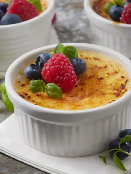 Nærbilde av tre skåler med crème brülée med friske bær på toppen. Foto til artikkel om sesongbaserte bryllupsmenyer.