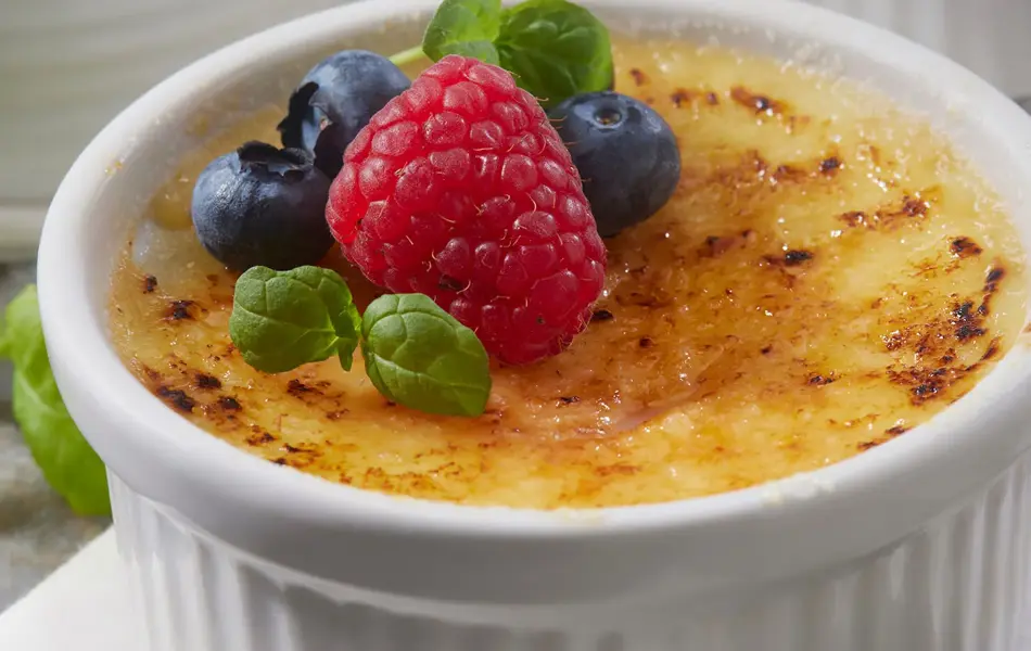 Nærbilde av tre skåler med crème brülée med friske bær på toppen. Foto til artikkel om sesongbaserte bryllupsmenyer.