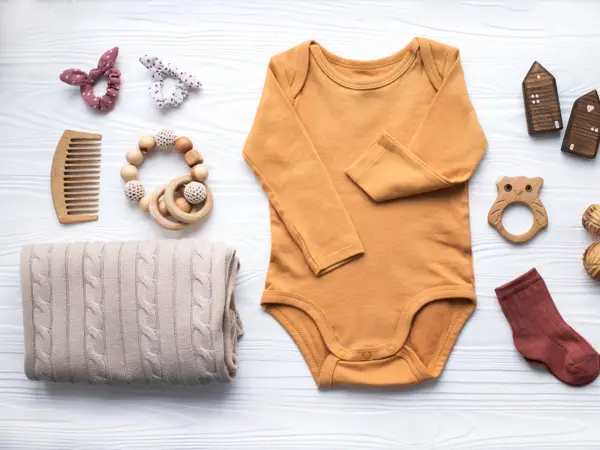 Newborn baby clothing, blanket, wooden toys, teether and accessories on white wooden background. Top view, flat lay.