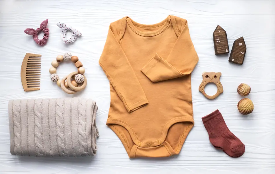 Newborn baby clothing, blanket, wooden toys, teether and accessories on white wooden background. Top view, flat lay.