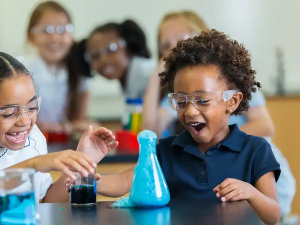 Diverse private school classmates are excited as foam overflows from beaker during chemistry experiment.