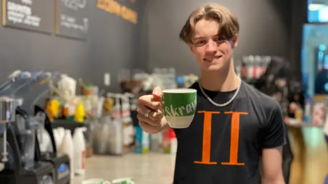 Mannlig ansatt hos Racoon coffe holder frem en skravlekopp