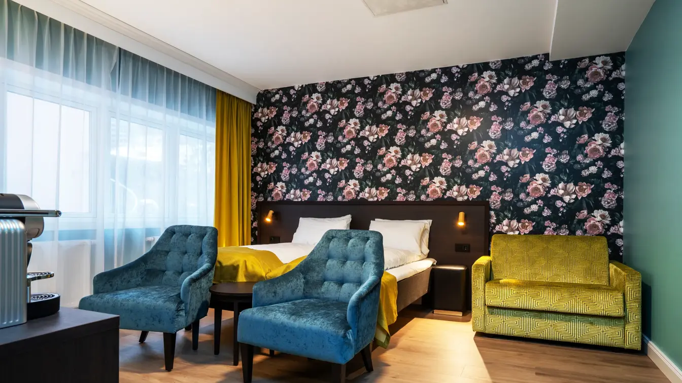  Blomstrete tapet med store lyserosa roser, dobbeltseng, lime grønn sofa, to turkise lenestoler og store vinduer. I superior rom på Thon Hotel Høyers i Skien.