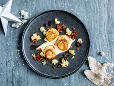 Tre stekte kamskjell dandert på en mørk tallerken 