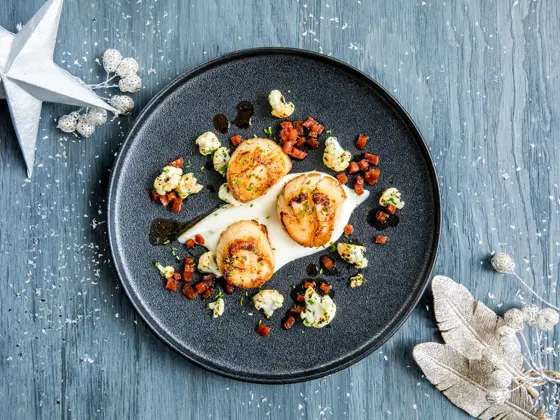 Tre stekte kamskjell dandert på en mørk tallerken 