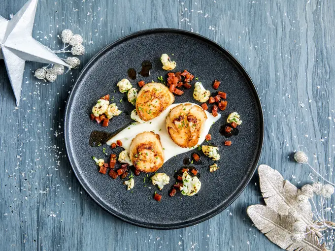 Tre stekte kamskjell dandert på en mørk tallerken 