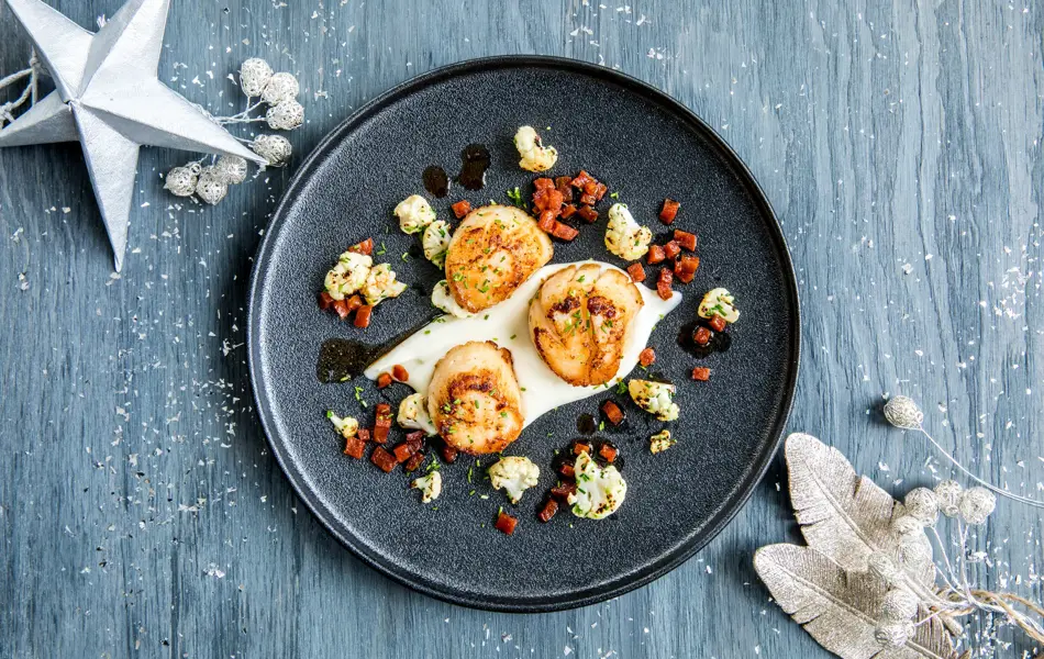 Tre stekte kamskjell dandert på en mørk tallerken 