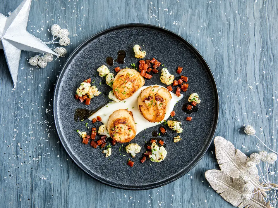 Tre stekte kamskjell dandert på en mørk tallerken 