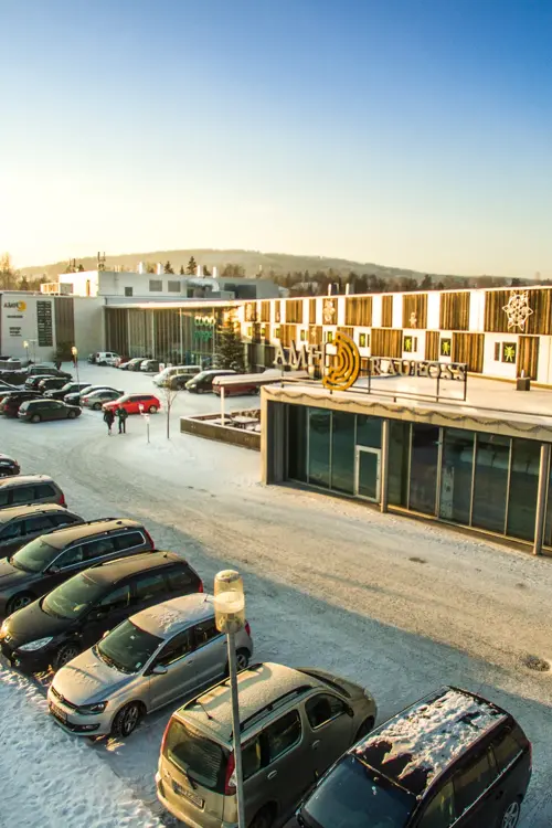 Fasadebilde av AMFI Raufoss viser biler parkert utenfor senteret om vinteren
