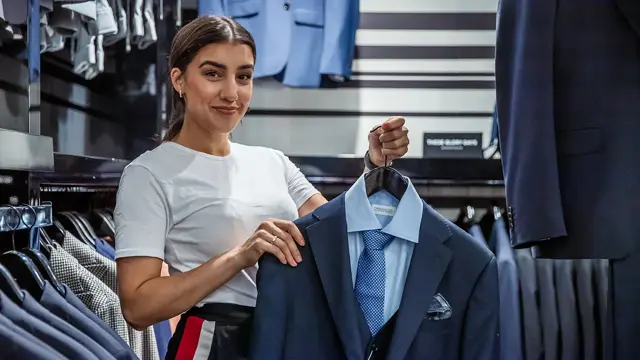 Bilde av en kvinnelig butikkansatt som holder en blå dress på henger