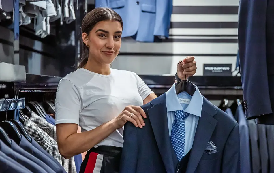 Bilde av en kvinnelig butikkansatt som holder en blå dress på henger