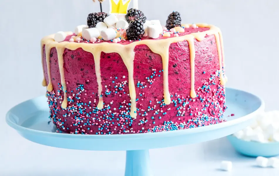 Rosa kake dandert med strøssel, minimarshmellows, bjørnebær, ballong og lys på blått fat