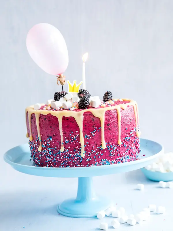 Rosa kake dandert med strøssel, minimarshmellows, bjørnebær, ballong og lys på blått fat