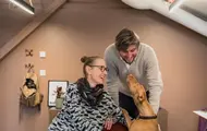 To ansatte i Global Ensemble Drama koser med en hund på kontoret 