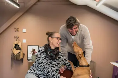 To ansatte i Global Ensemble Drama koser med en hund på kontoret 