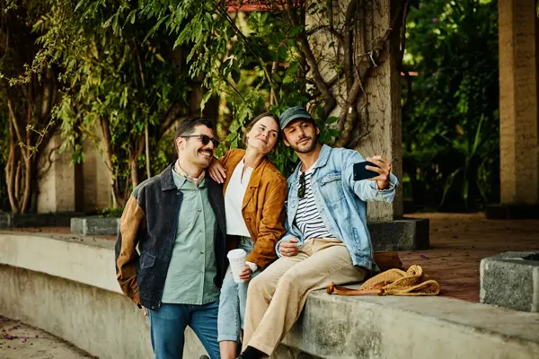 Tre venner tar selfie sittende på en murvegg 